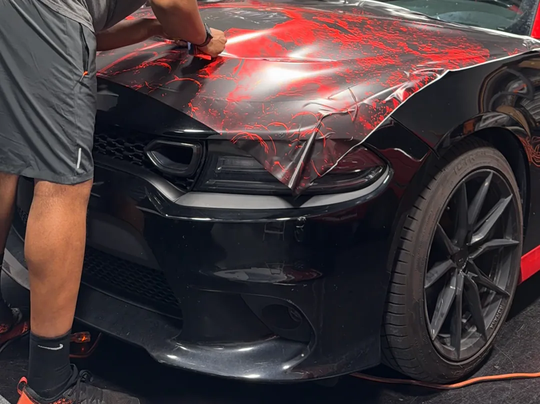 Installer squeegeeing a patterned hood wrap on a Dodge Charger